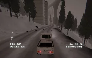 A car is driving through a snow filled path with trees, buildings and a high bridge in the back. 